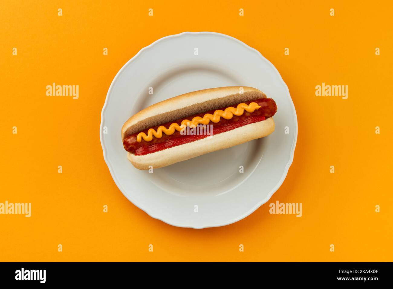 Classic hot dog with wurst, ketchup and mustard on orange background