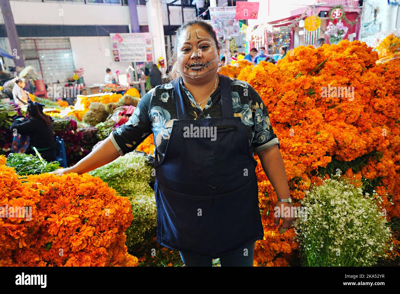Mexico City, Mexico. 31st Oct, 2022. A vendor wearing face paint stands with her pile of cempasuchil flowers, the traditional Day of the Dead flower used to decorate altars and gravesites during the annual festival at the Jamaica Flower Market, October 31, 2022 in Mexico City, Mexico. Credit: Richard Ellis/Richard Ellis/Alamy Live News Stock Photo
