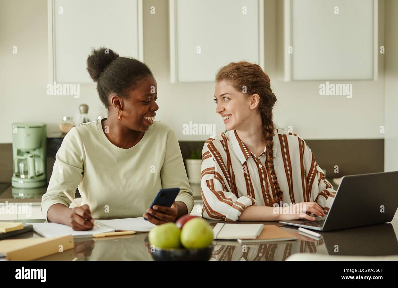 Portrait of two young women looking at each other and smiling while working on small business ideas together at home Stock Photo
