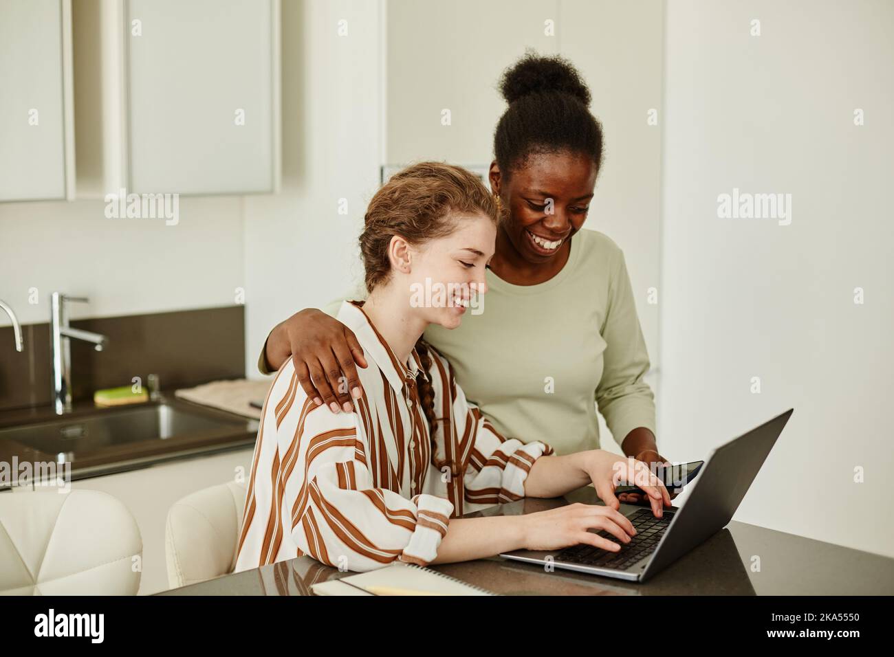 Portrait of two smiling young women using laptop together at home while managing small business or studying online Stock Photo