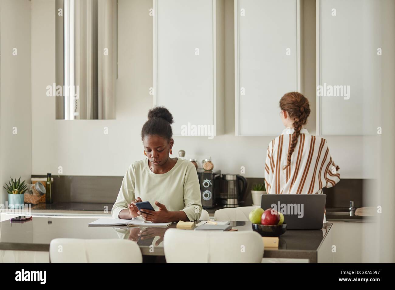 Minimal portrait of young black woman using smartphone while working from home in kitchen interior copy space Stock Photo