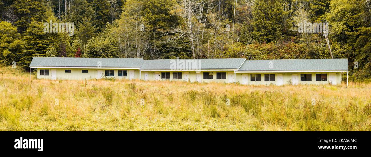Old abandonded single story motel with long grass on woodland edge with no people Stock Photo