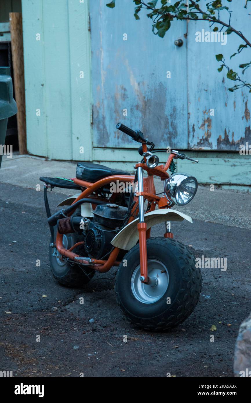 An Orange motorcycle parked on a side road behind a wooden building. Stock Photo