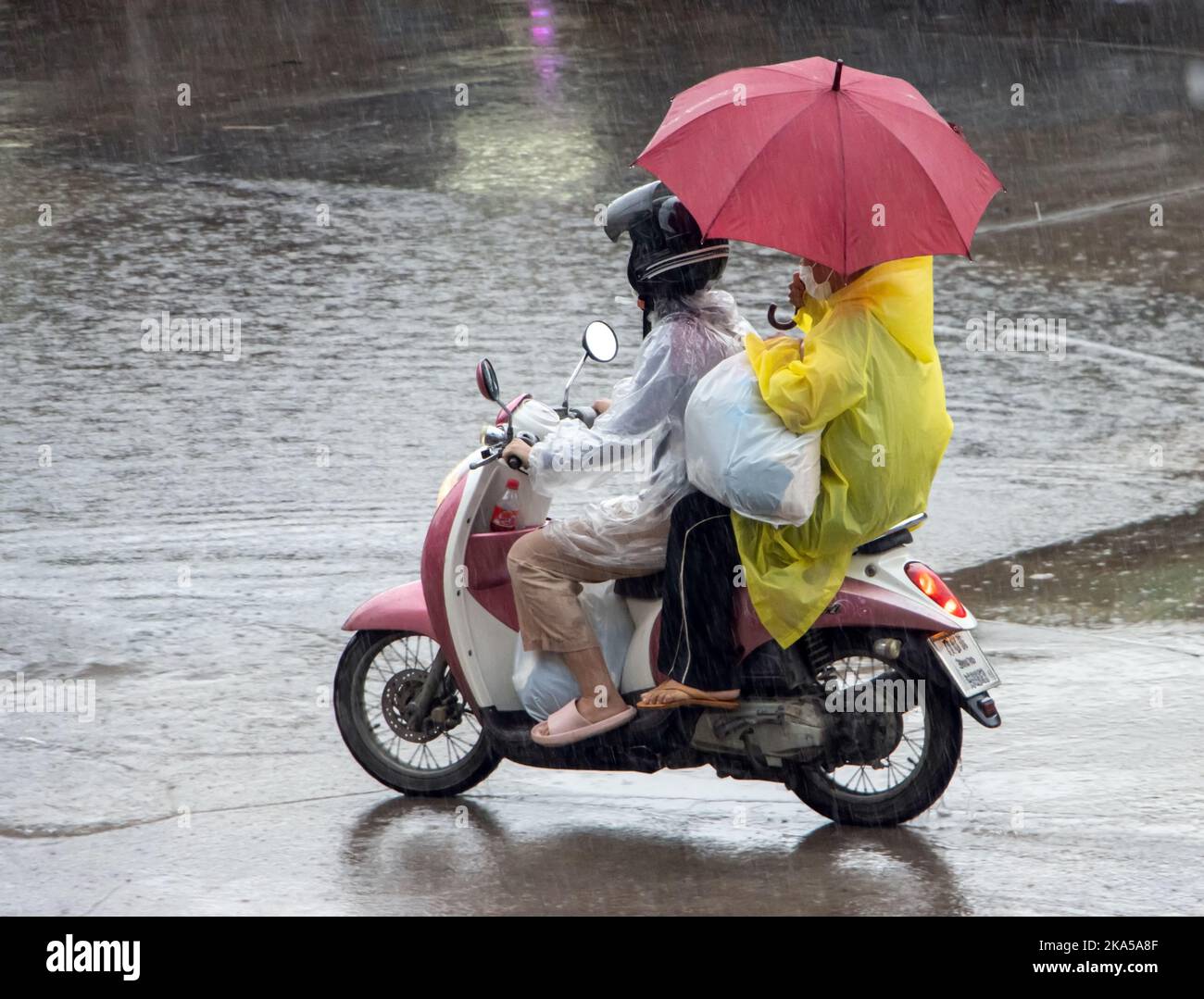 A couple with an umbrella is riding a motorcycle in the rain Stock