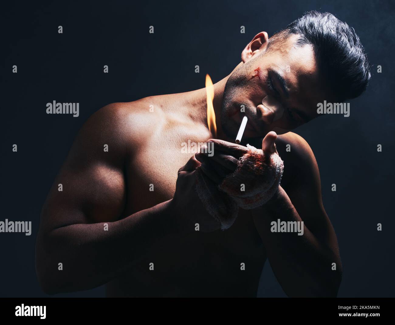 Dark, flame and man lighting a cigarette with a lighter to smoke after a fight in a studio. Young, dangerous and smoker or fighter from Puerto Rico Stock Photo