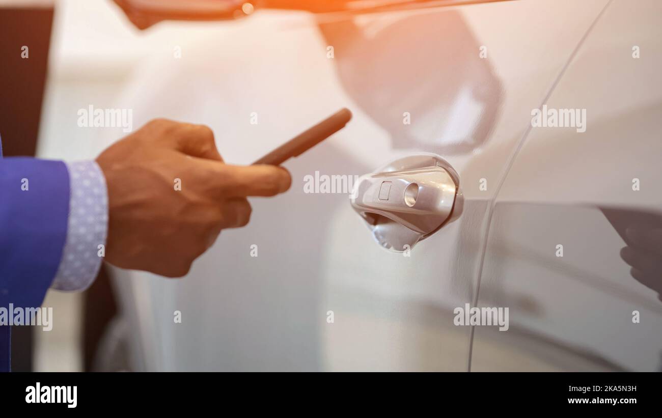 Black salesman opens car using app on mobile phone Stock Photo