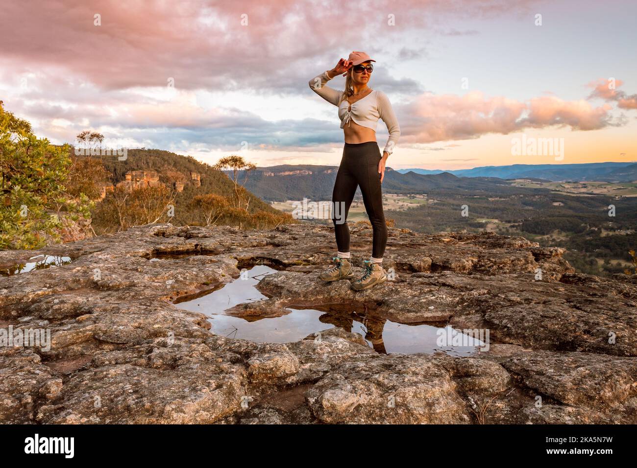 A female stands on a rock plateau in Blue Mountains as the sun sets Stock Photo