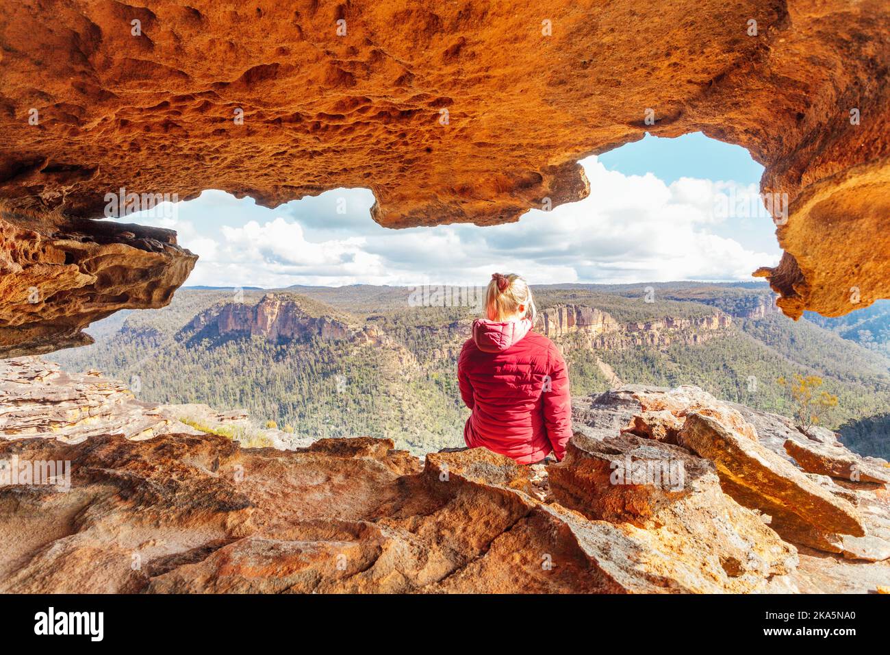 Woman sits in a sandstone  cave with spectacular mountain views Stock Photo