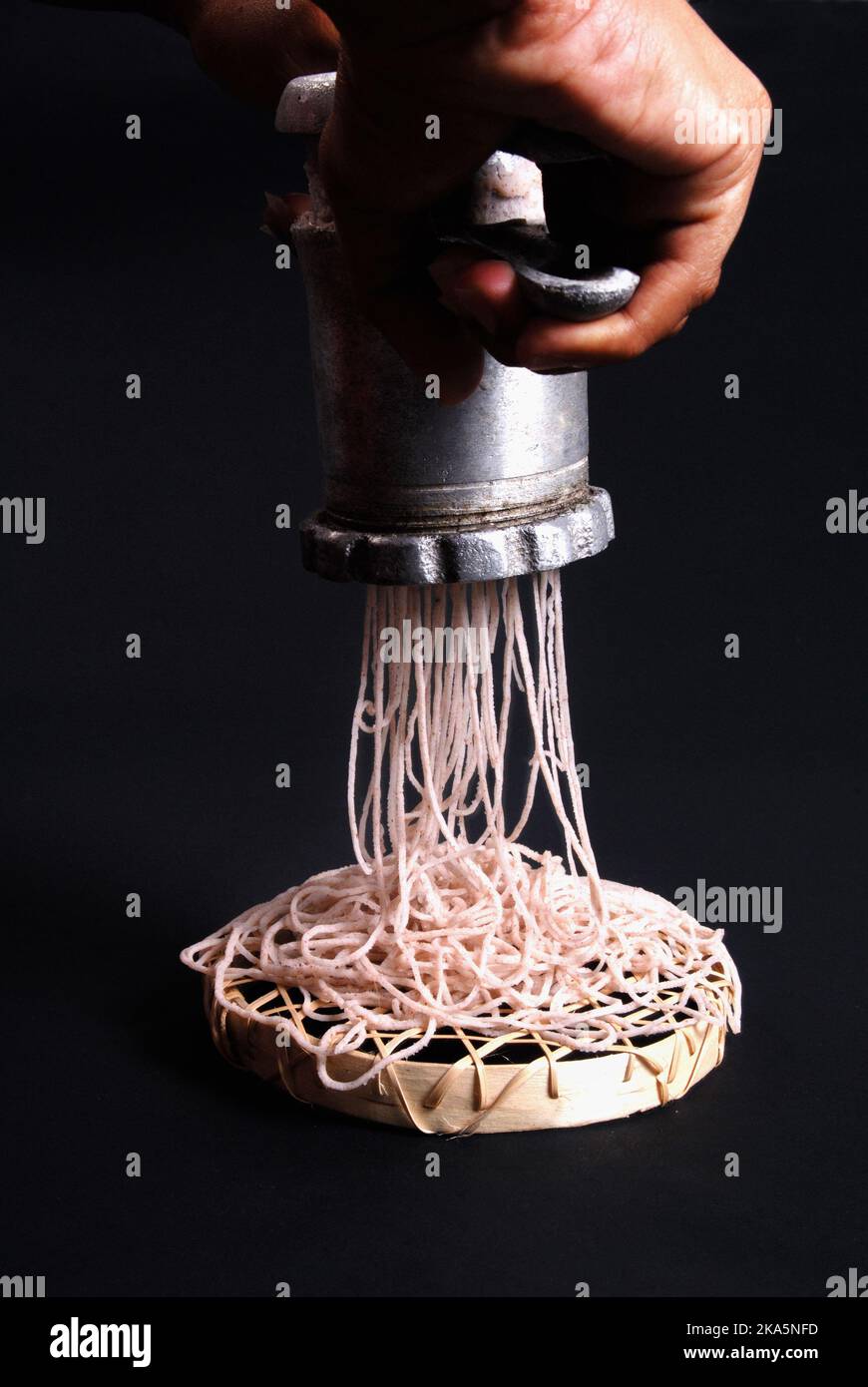 Home brew string hoppers. Lady making string hoppers using traditional equipment and flour. Lady hands and equipment in black background sri lanka. Stock Photo