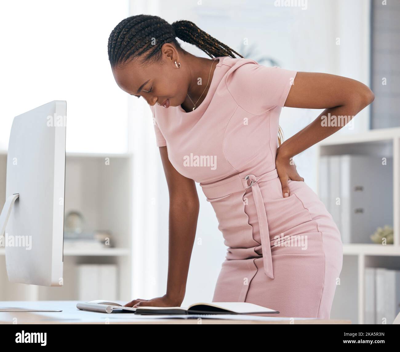 Back pain, bad posture and strain with a black woman in business suffering while working at her desk in the office. Anatomy, spine and cramp with a Stock Photo