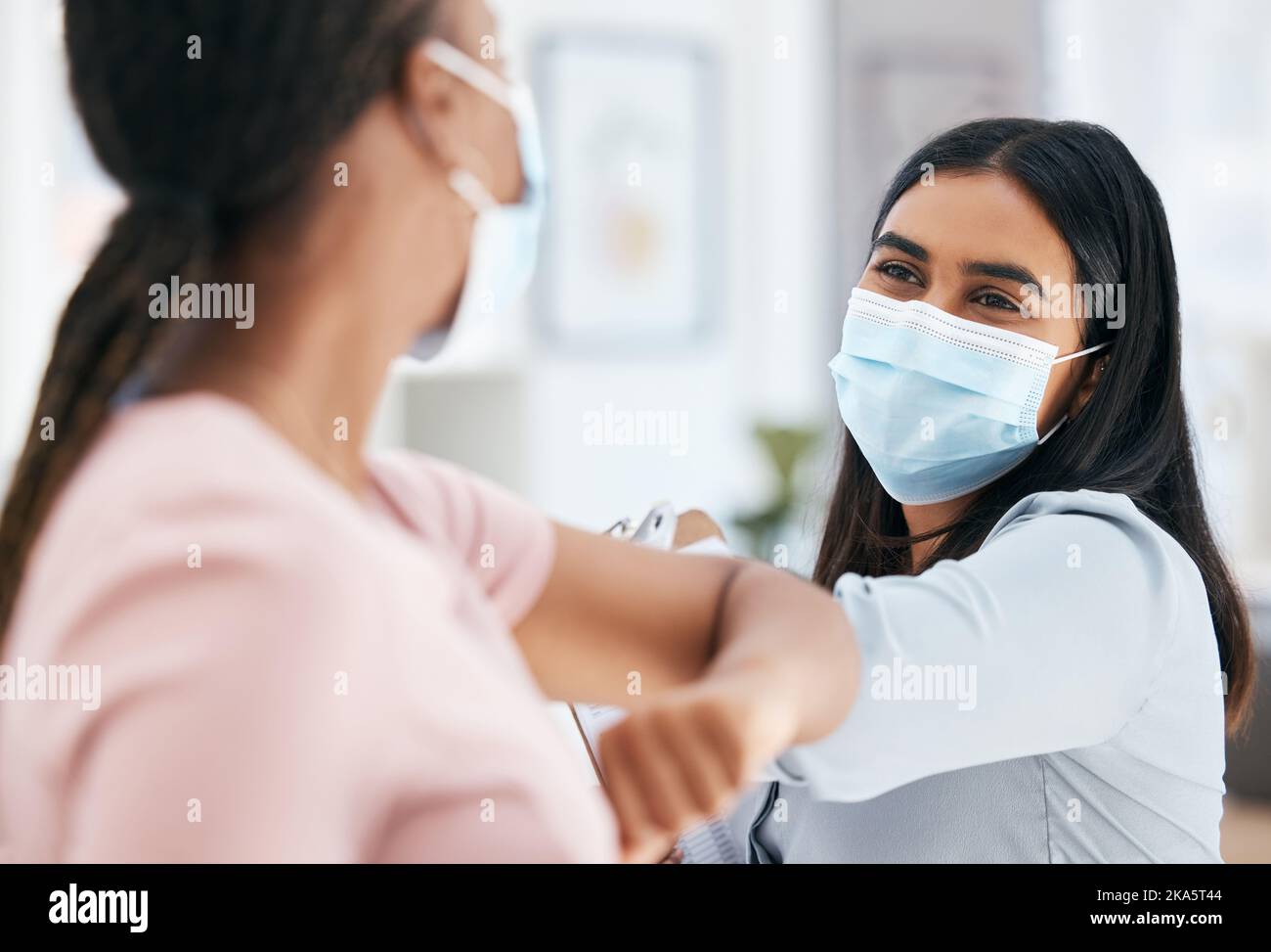 Covid, elbow bump and employees greeting while wearing face mask in office for teamwork and collaboration. Business women social distancing during Stock Photo