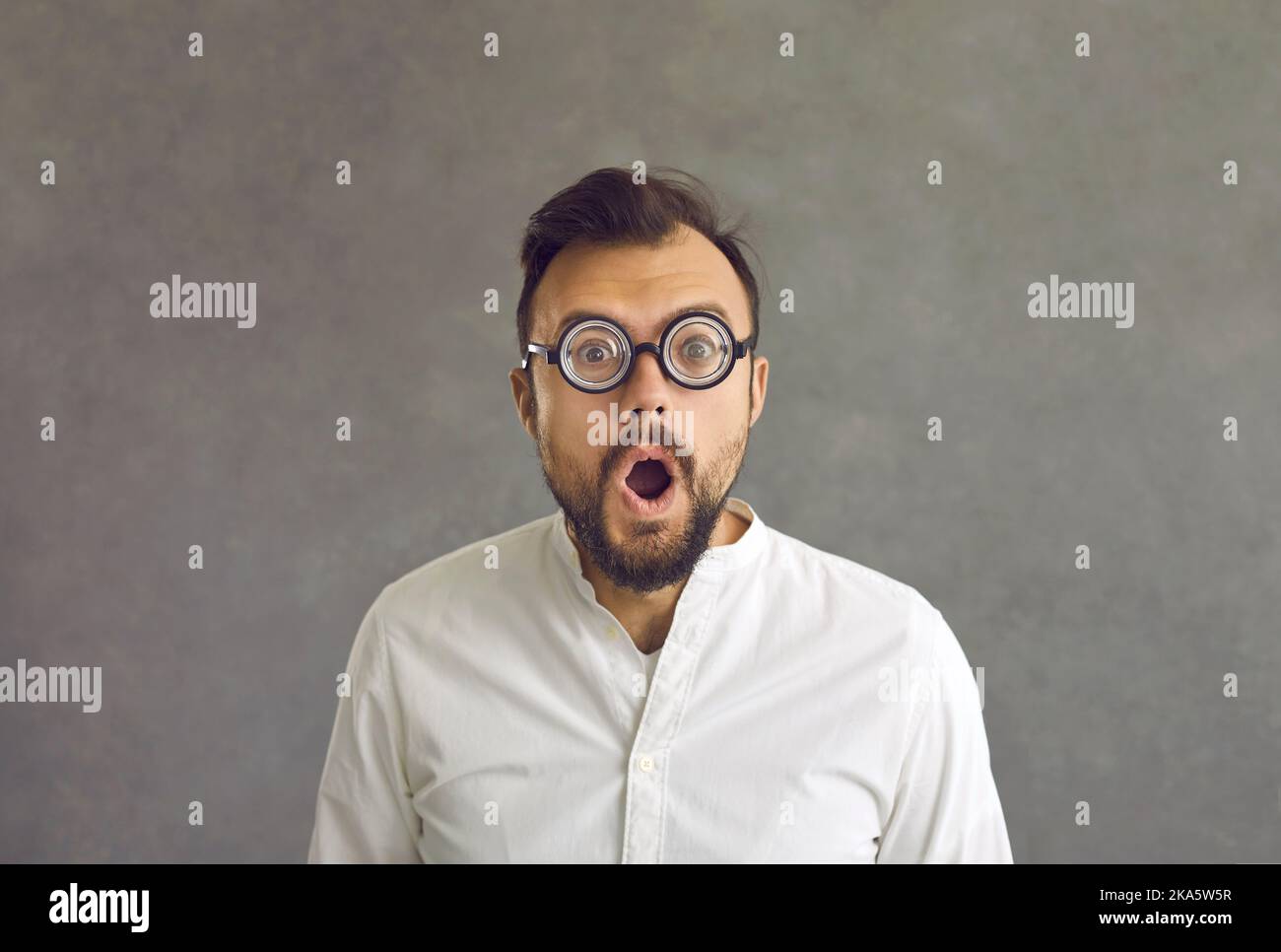 Portrait of funny shocked man round optical glasses standing on grey background Stock Photo