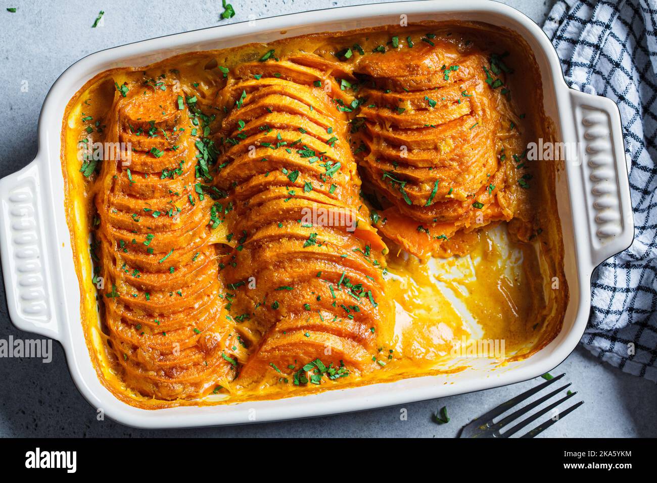 Roasted sweet potato gratin with parsley in a ceramic pan, top view