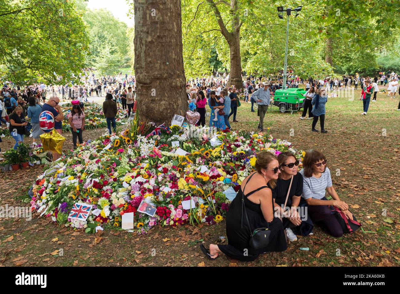 Three women posing for photo in front of the  floral tributes, left by mourners in Green Park to mark the Queen Elizabeth II death. Green Park, London Stock Photo