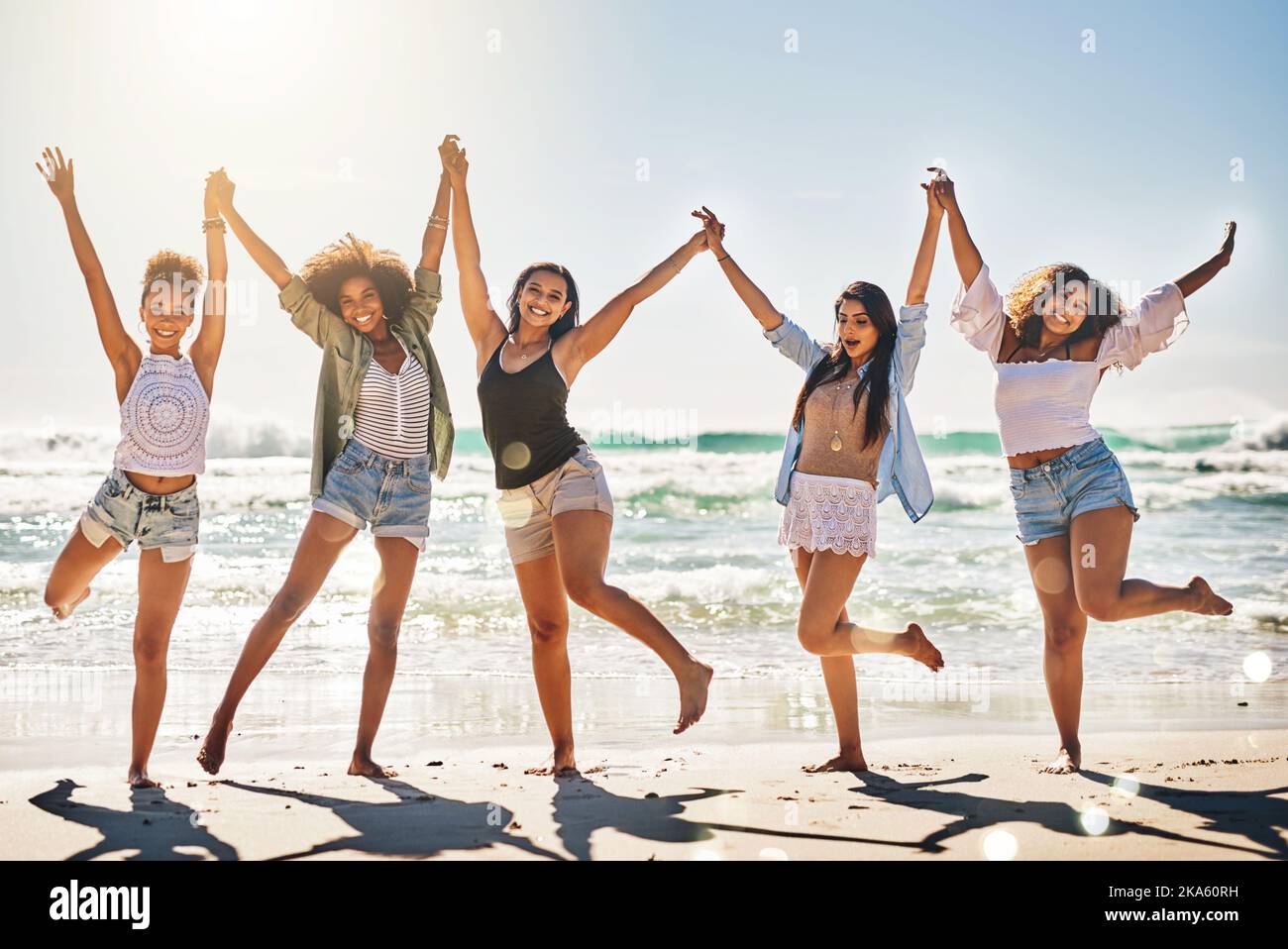 They have an unbreakable bond. a group of cheerful friends holding hands on the beach. Stock Photo