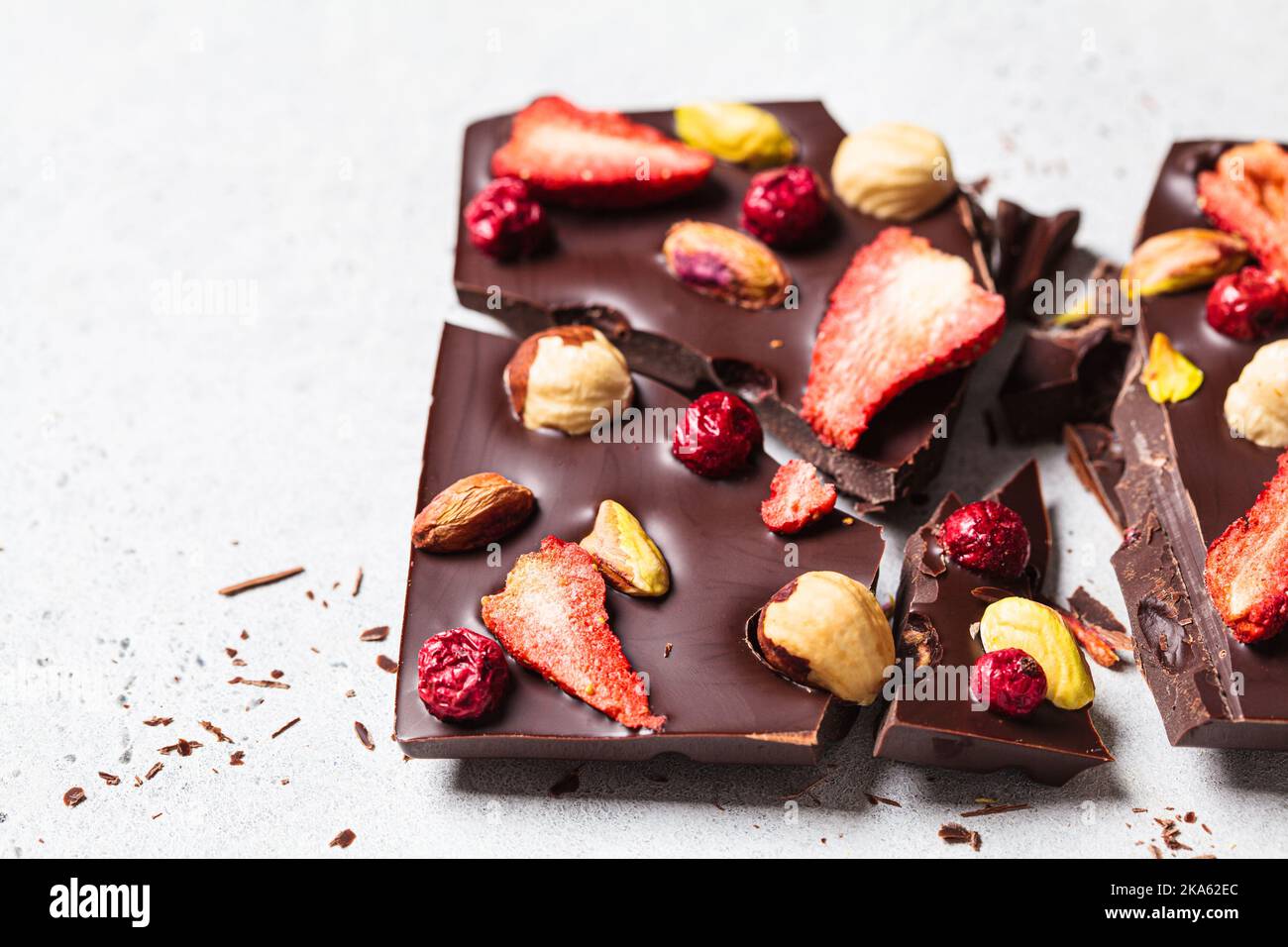 Vegan homemade dark chocolate with berries and nuts on white paper, copy space. Stock Photo
