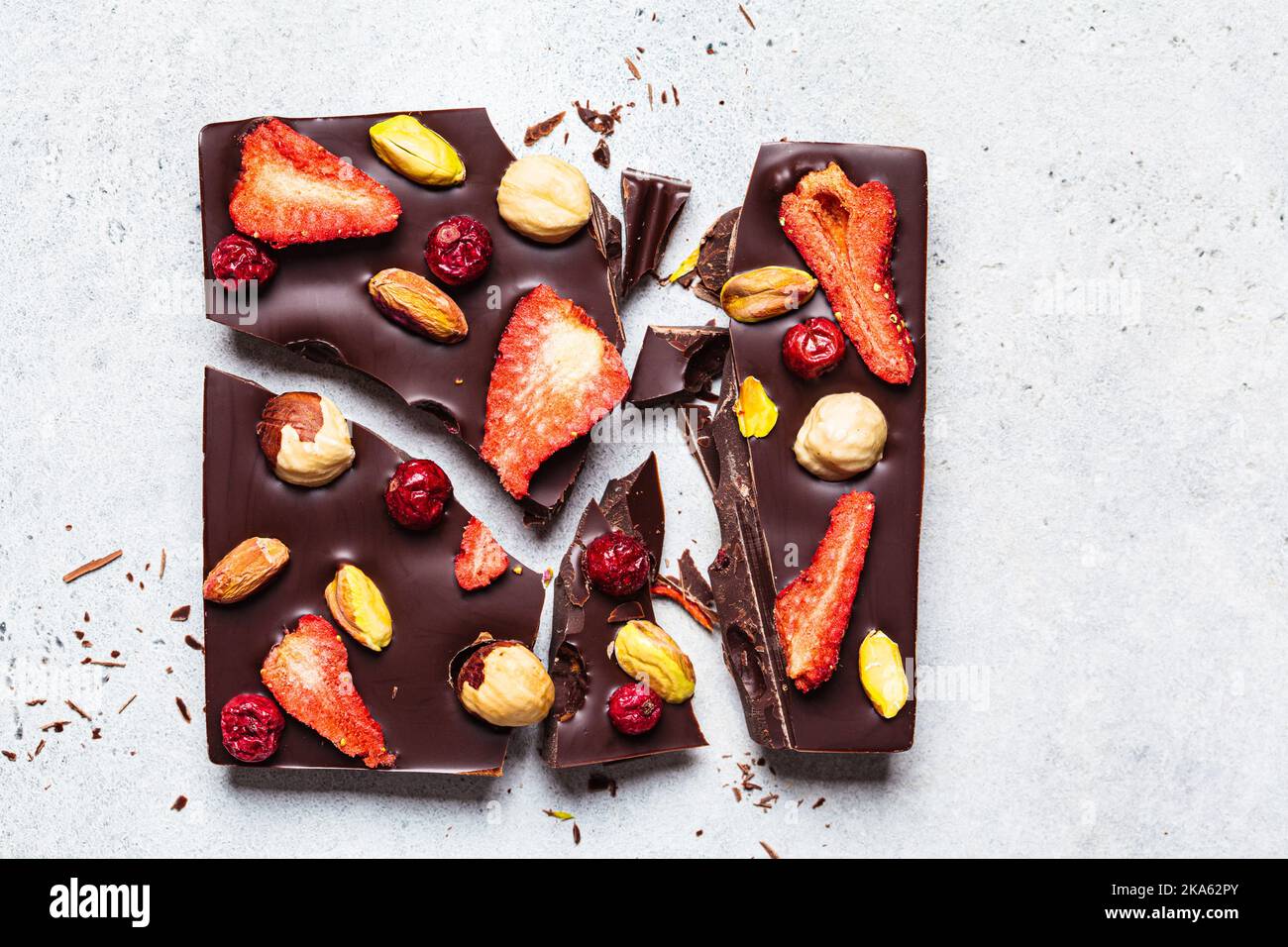 Vegan homemade dark chocolate with berries and nuts on white paper, top view. Stock Photo