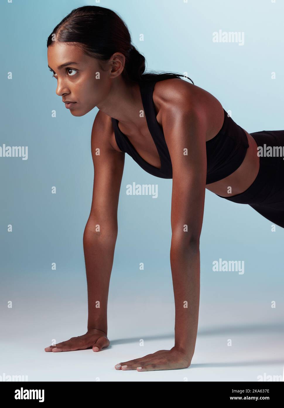 Fitness, exercise and focus with a sports woman in studio on a blue background doing pushups for strong muscles. Training, health and workout with a Stock Photo