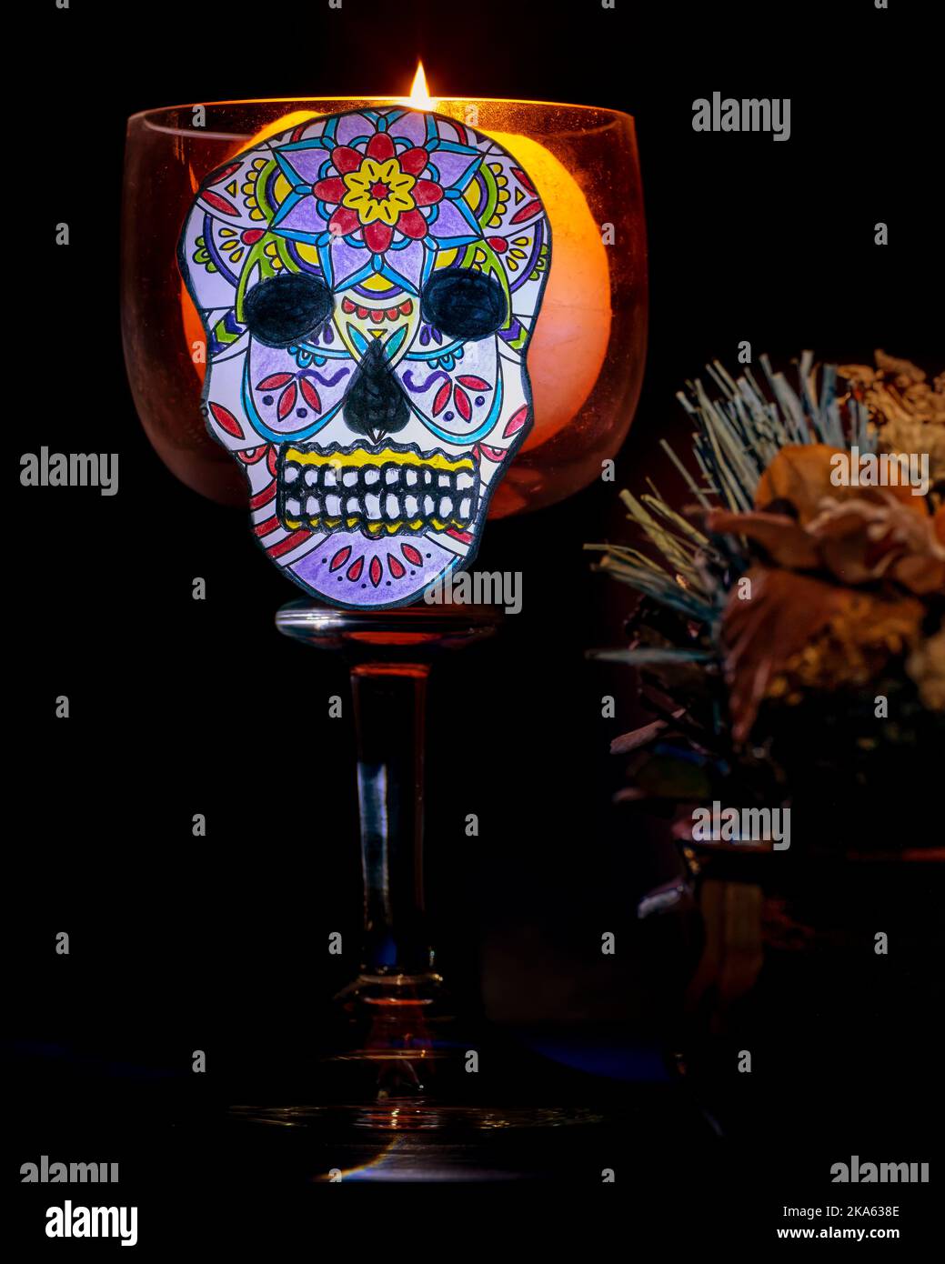 A characteristic calavera, which in Mexican tradition celebrates the day of the dead, with a lit candle next to it Stock Photo