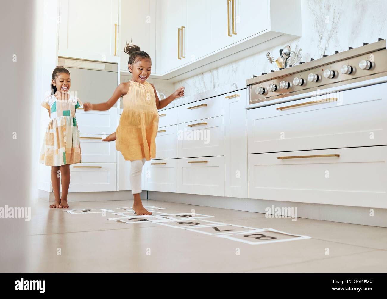 Hopscotch, fun and children playing a game together in the kitchen of their modern family home. Happy, smile and girl kids or sisters jumping on Stock Photo