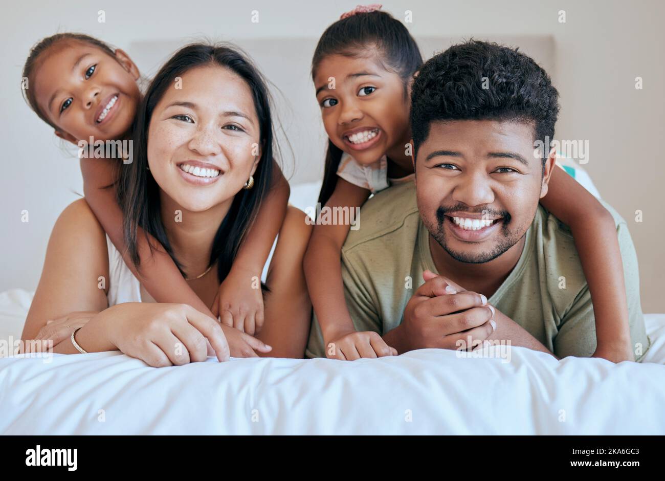Happy family, bed and girl with mother, father and sister in a bedroom for fun, bond and rest together. Face, portrait and mexican family hug, smile Stock Photo