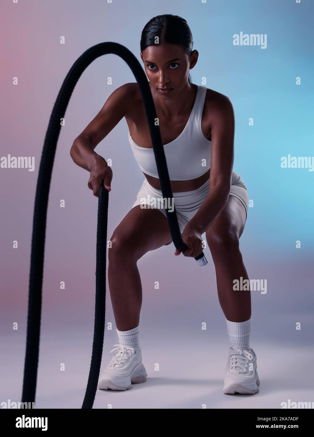 Girl, fitness and rope training exercise for cardio, muscle and endurance practice with color studio background. Focus, health and power of Indian Stock Photo