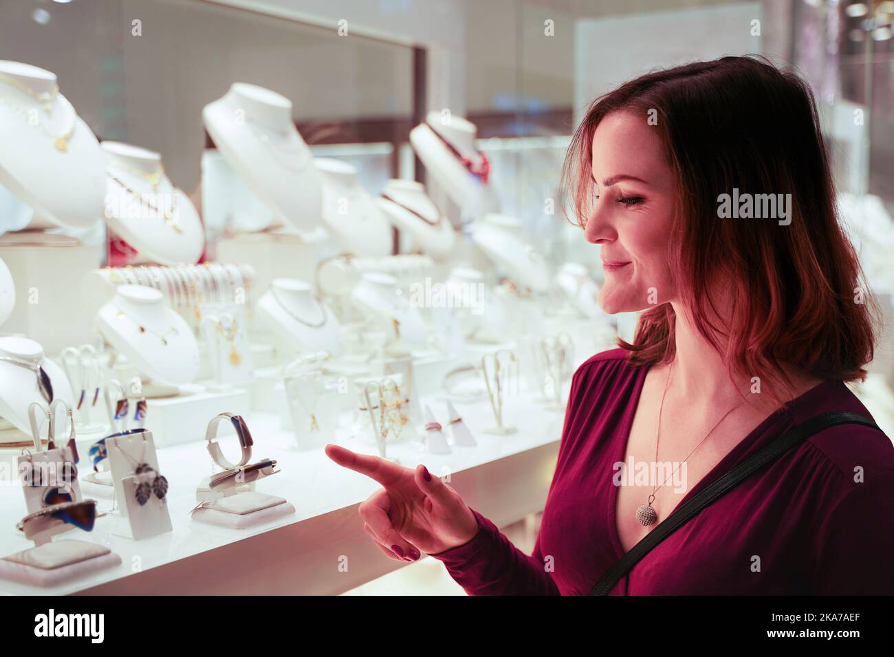 Pretty woman looking at jewelry in store window. Girl near jewellery. Interested customer chooses gold, diamonds or precious stones. Stock Photo