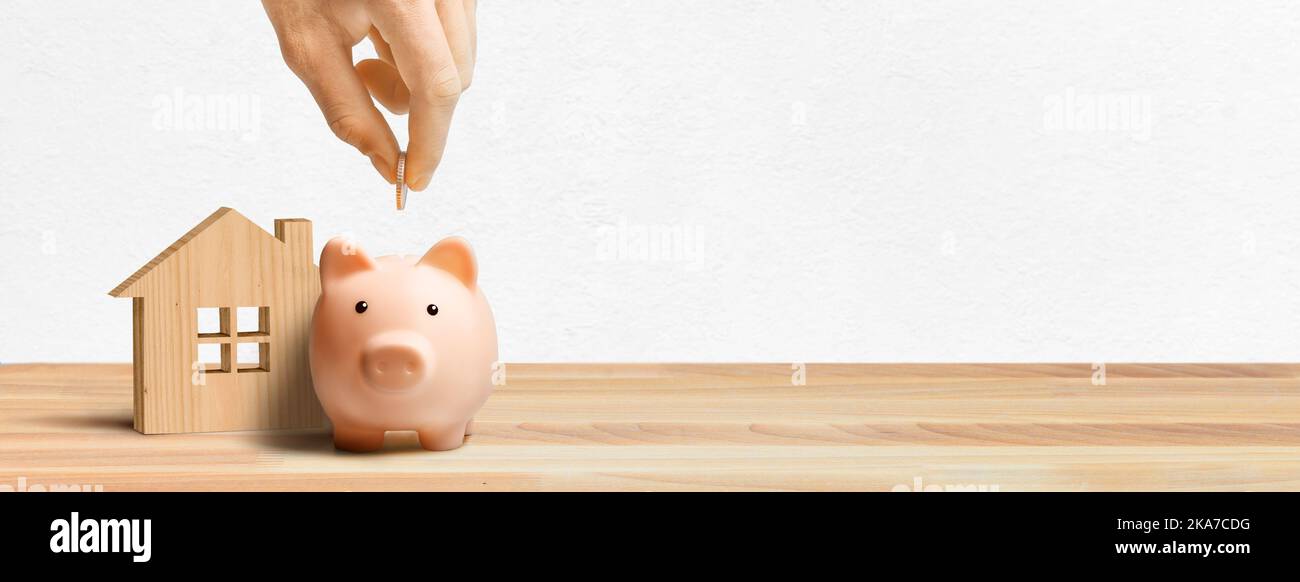Wooden House model and piggy bank on the table near white wall Stock ...