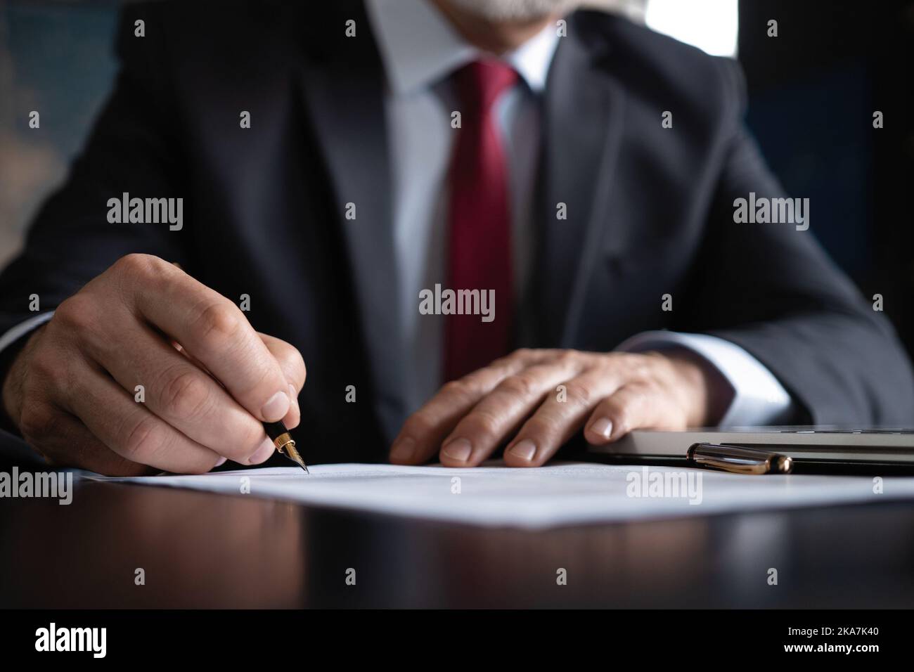 Mature businessman signs documents with a pen making the signature sitting at the desk Stock Photo
