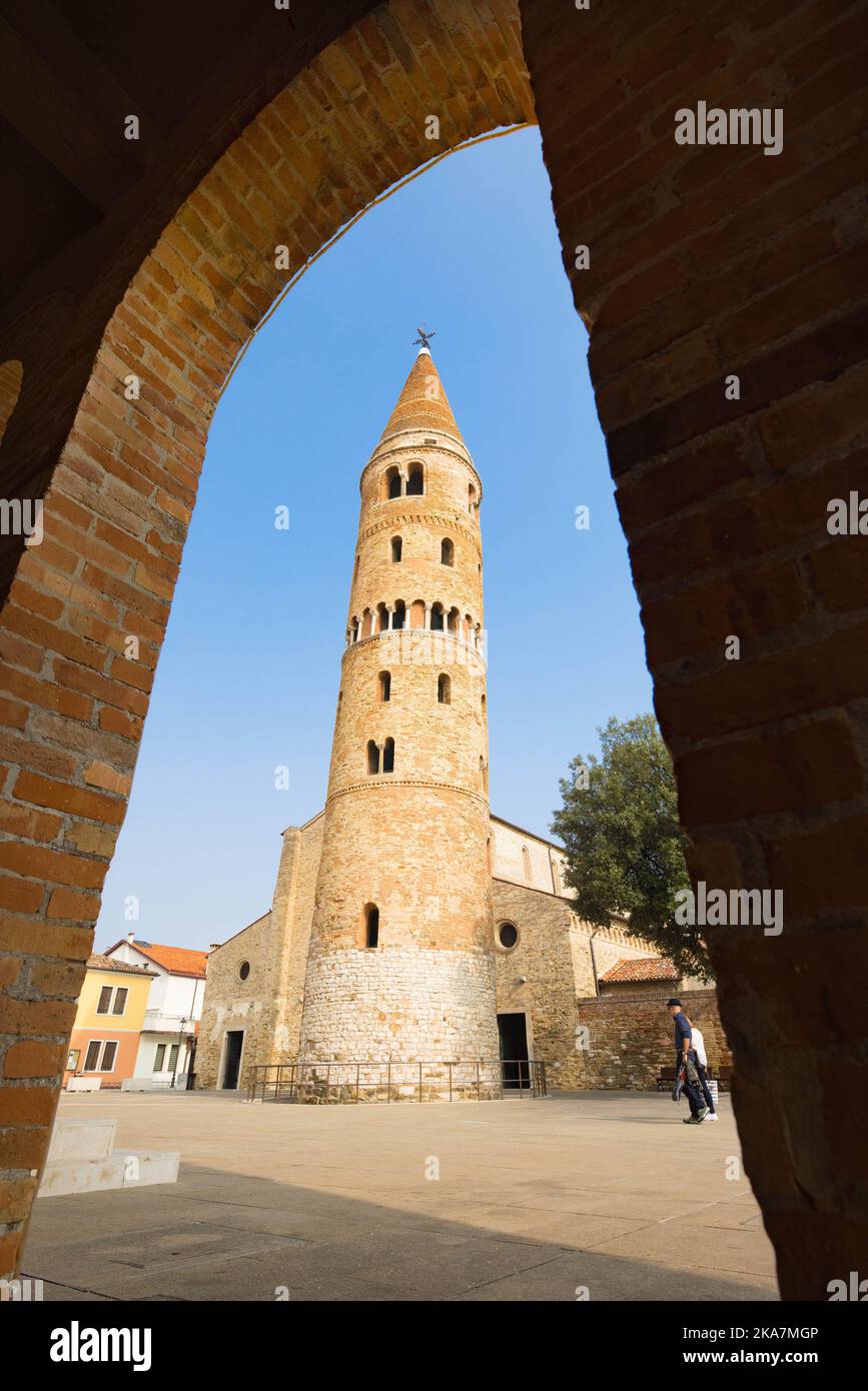 Caorle Cathedral Tower and cathedral church behind it during sunny day and blue sky seen from under an arch Stock Photo