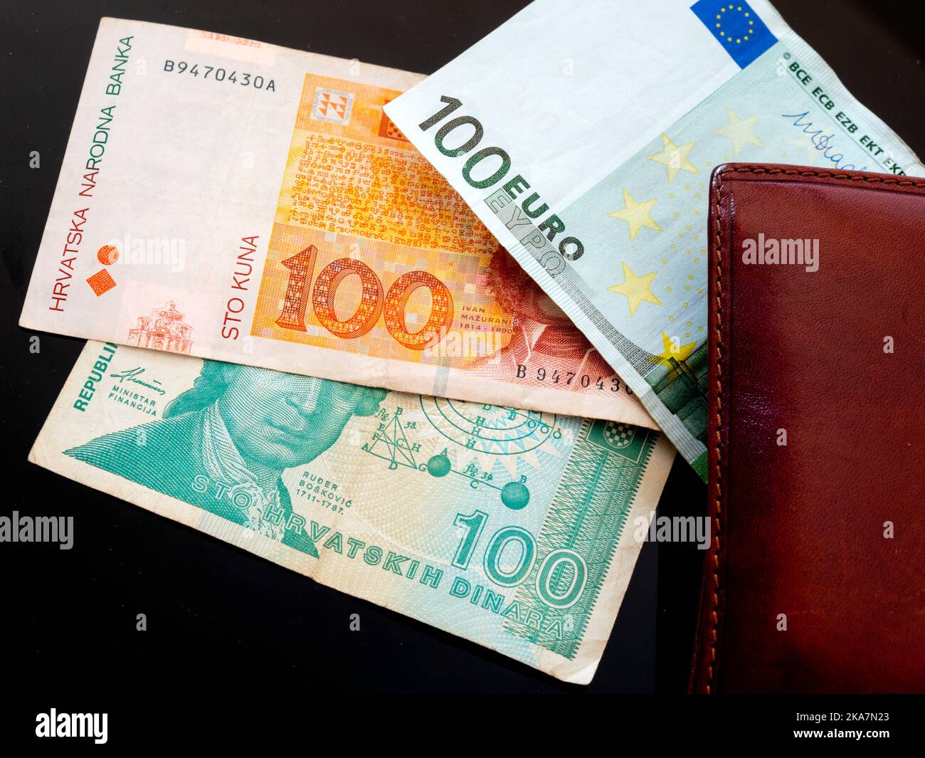 Paper money peering from wallet brief Croat Croatia banknotes of 100 Croatian Dinars Kuna Kune Kunas and EU Euro Euros on Black background Stock Photo