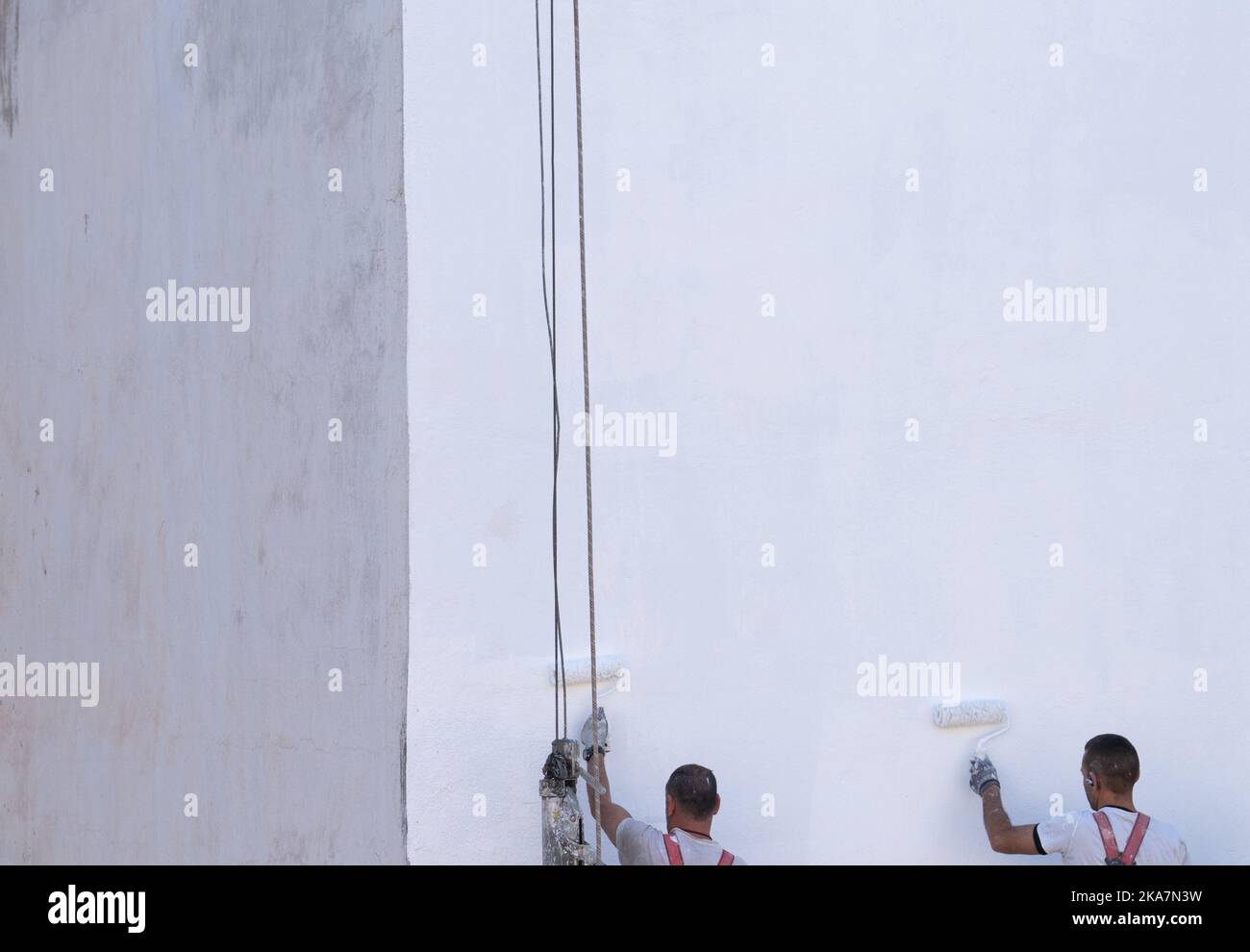Unrecognizable painters painting the wall in white on scaffolding Stock