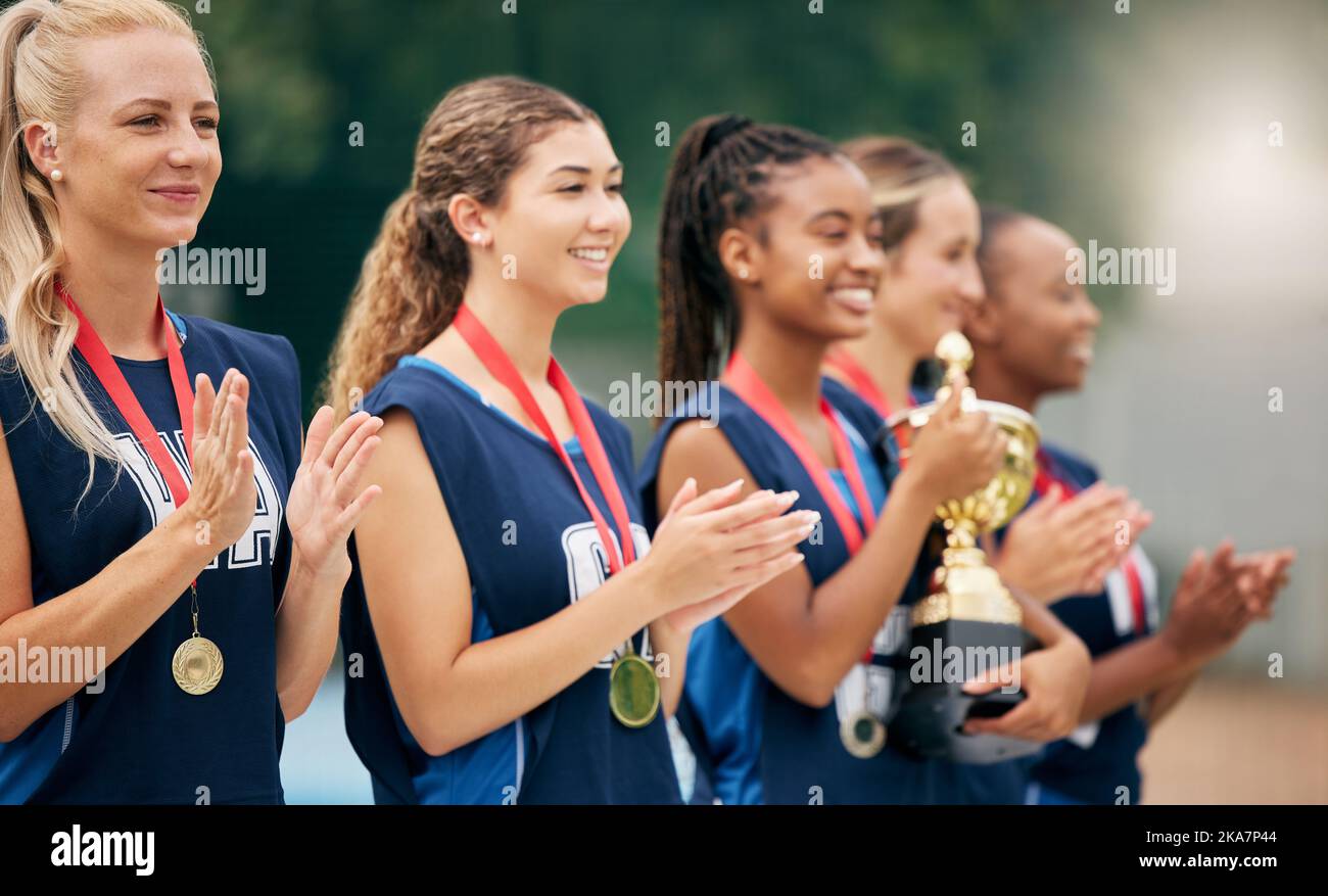 Netball team, clapping and medal, trophy and winner in sports competition, tournament and game outdoor. Teamwork, support and gold award for Stock Photo