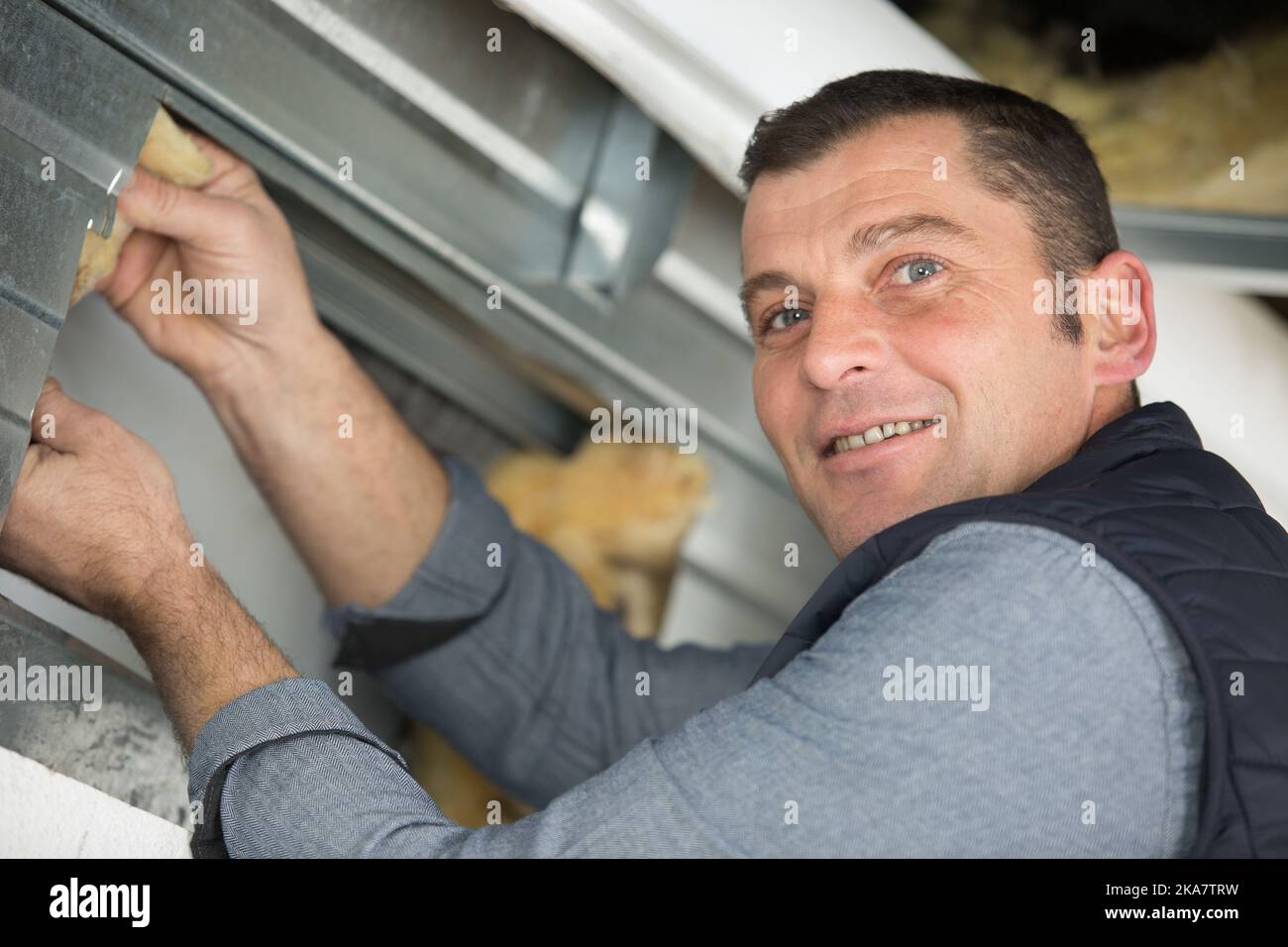 man inserting insulation behind a metal framework Stock Photo - Alamy