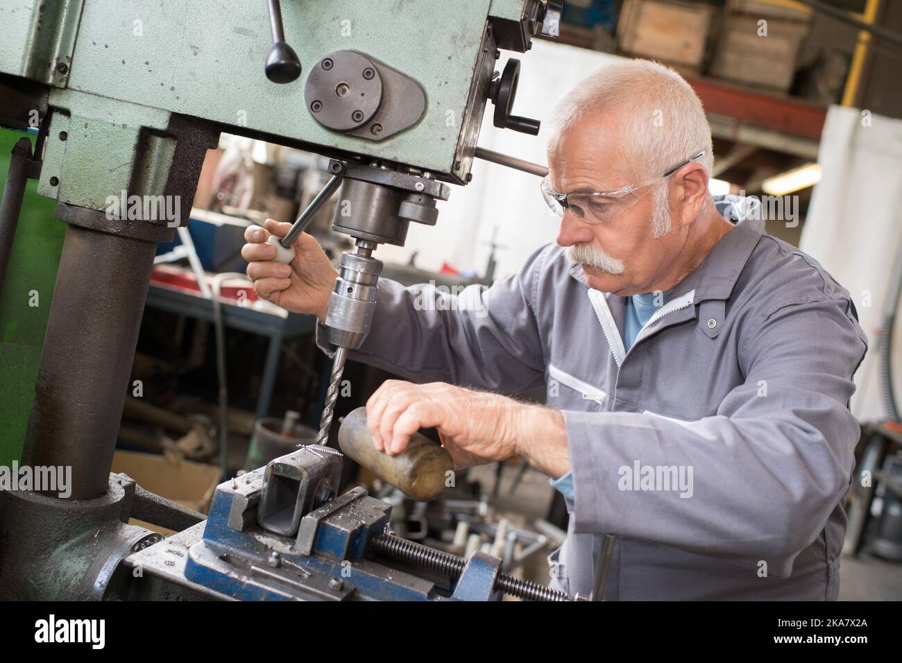senior metal worker using industrial drilling machine in workshop Stock Photo