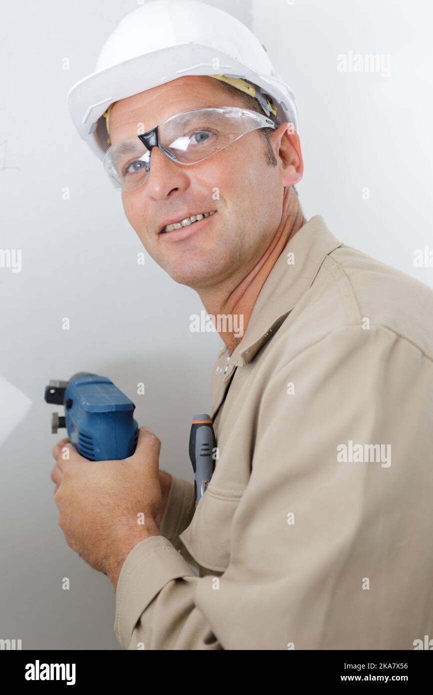 mature builder using drill on wall Stock Photo