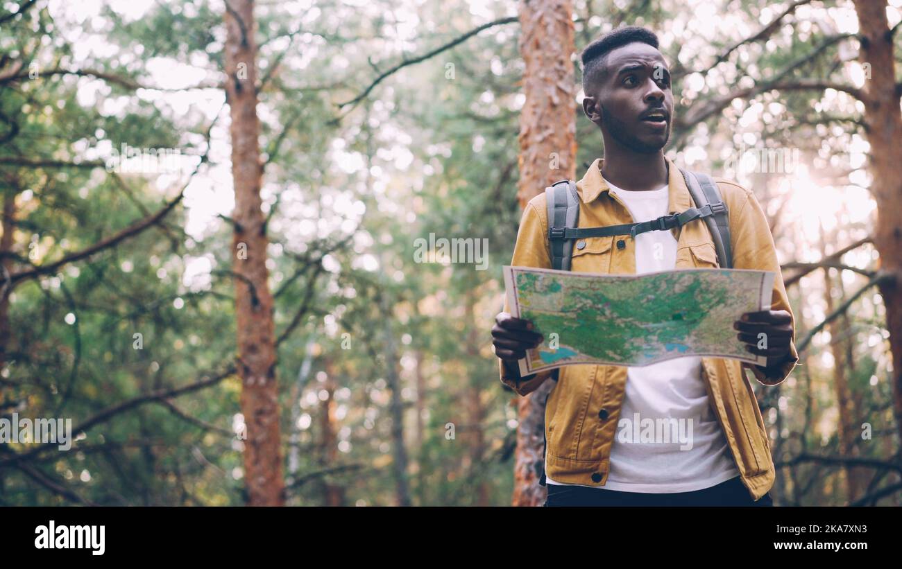 African American man is walking in forest looking at paper map searching for desired tourist destination . Nature, active lifestyle and navigation concept. Stock Photo