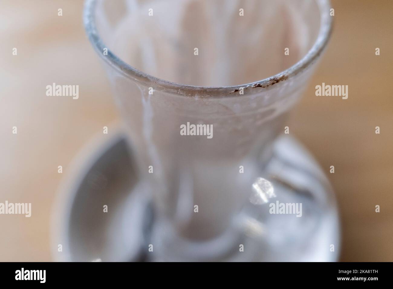 A closeup view of the rim of a used latte glass in a saucer on a table. Stock Photo