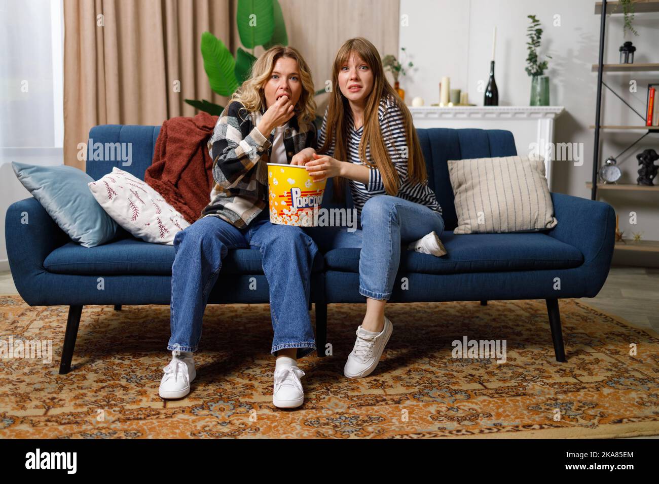 Women with surprised faces watching tv at home on the couch Stock Photo