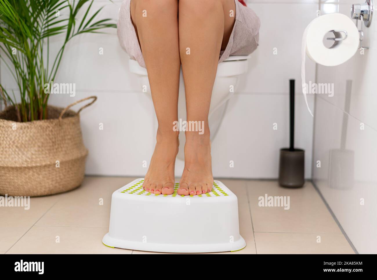 Woman sitting on the toilet and propping her feet on a footstool Stock Photo