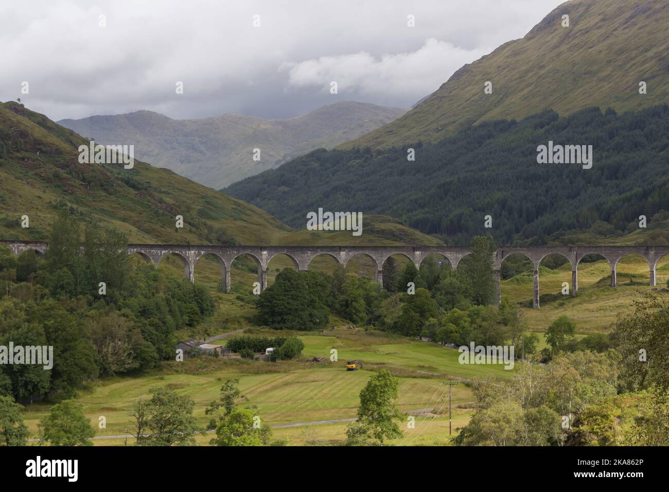 An aerial view of Glenfinnan Viaduct bridge surrounded by dense forest  and greenery fields in Scotland Stock Photo