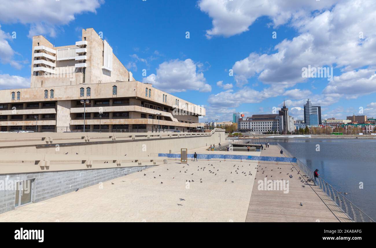 Kazan, Russia - May 6, 2022: Galiaskar Kamal Tatar Academic Theatre exterior. Street view, ordinary people walk the coast of Lake Kaban on a sunny day Stock Photo