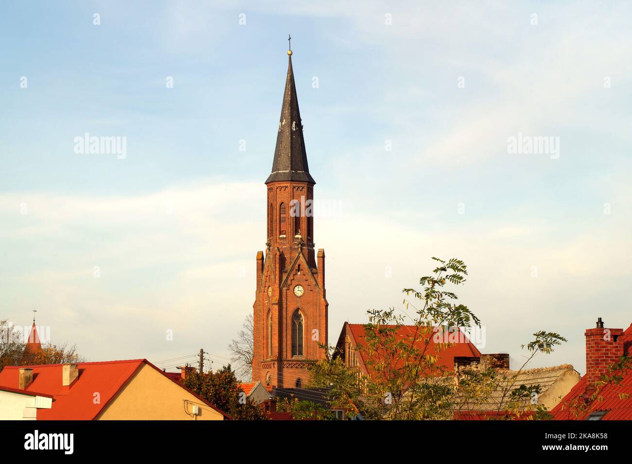 In the photo, among the roofs of houses, the spire of the church tower with a cross, against the background of a blue sky. horizontal photo taken in t Stock Photo