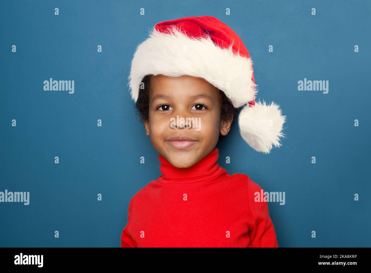Curious black kid portrait. Little child boy in Santa hat smiling on blue background Stock Photo