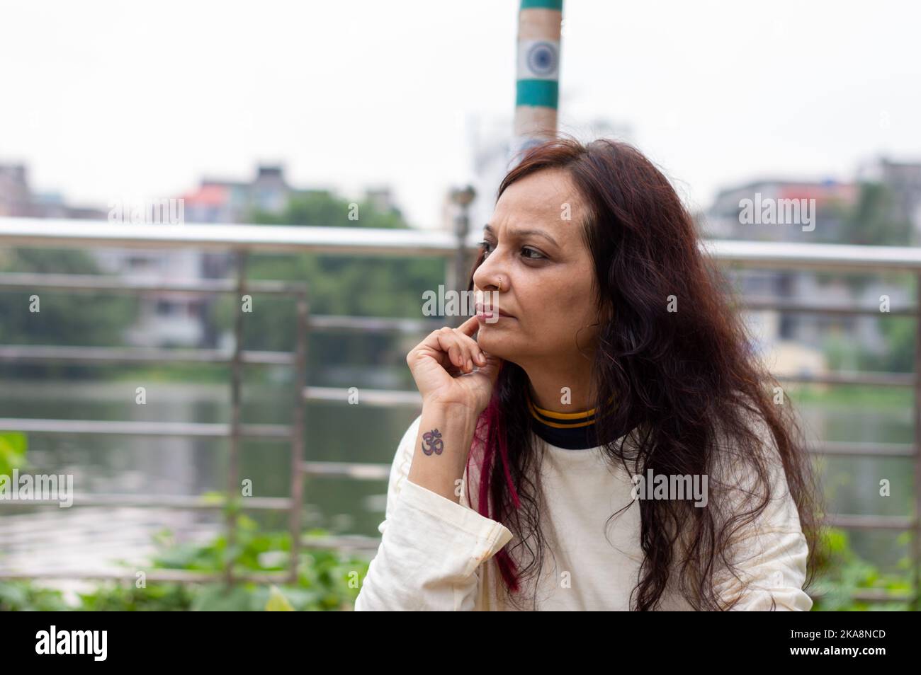 Mid Adult worried Woman sitting on hand on chin pose in a park bench and looking at a distance. Front view. Indian Ethnicity Age 50 to 54 Years. Stock Photo