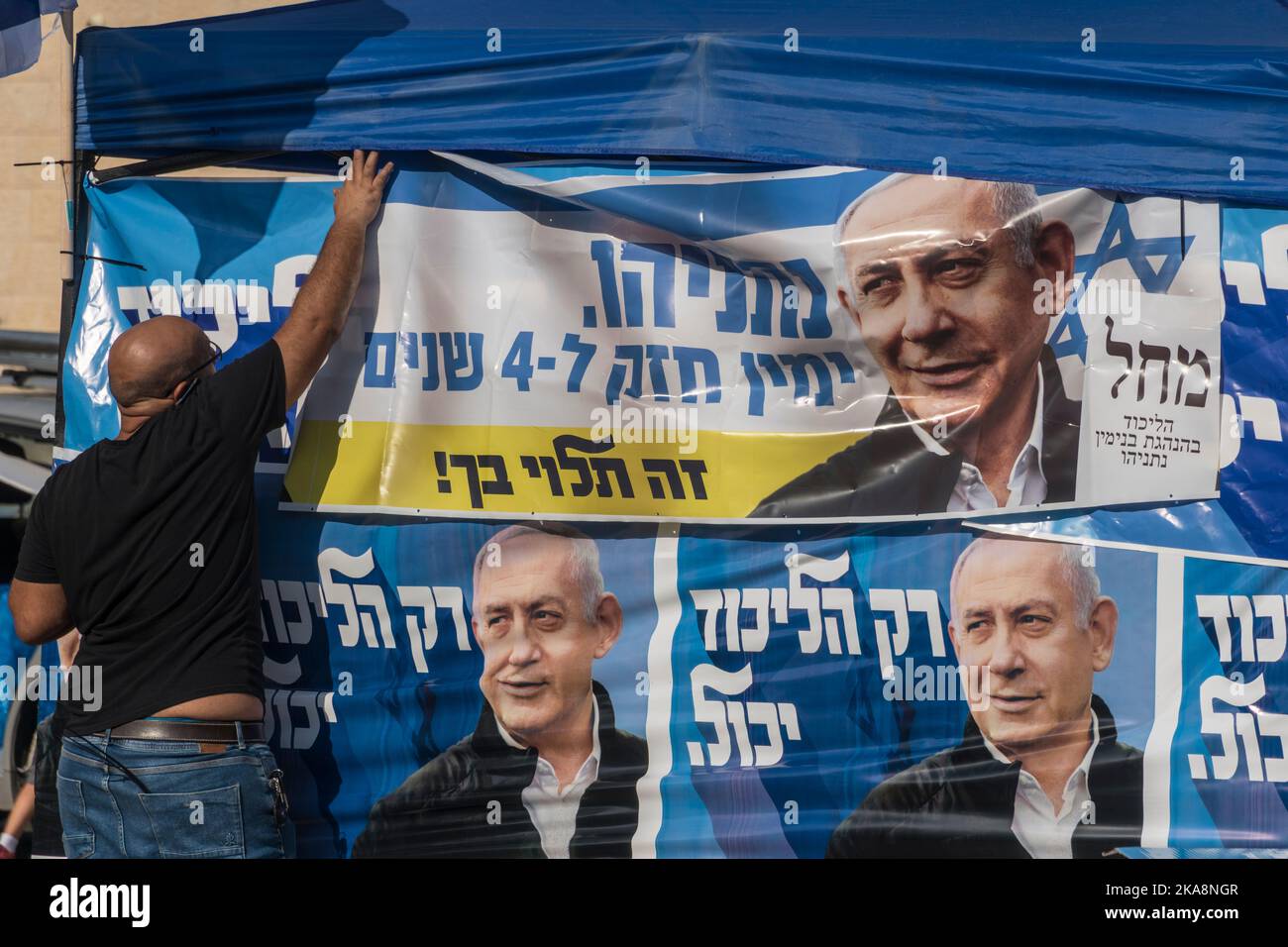 A man straightens a poster of opposition's leader Benjamin 'Bibi' Netanyahu and his 'Likud' (Unity) party on a booth near a voting station in the city of Harish, as Israel votes for the 5th time since 2019. Stock Photo