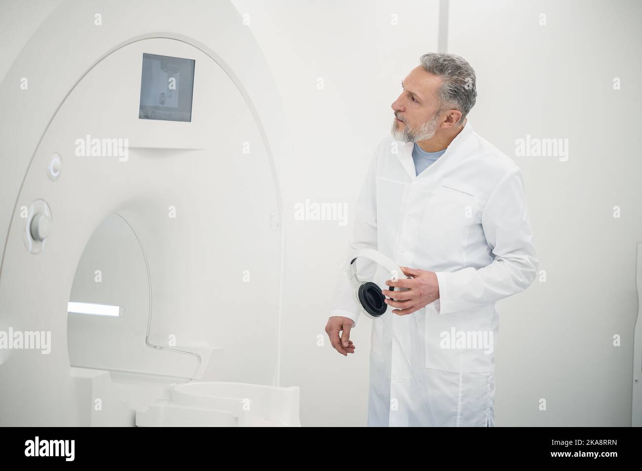 Male gray-haired doctor in a lab coat near MRI scanner Stock Photo