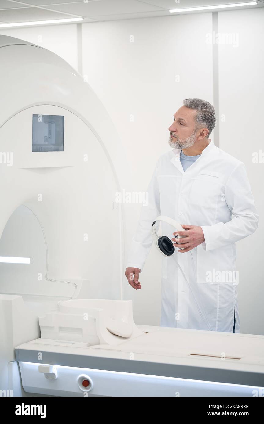 Male gray-haired doctor in a lab coat near MRI scanner Stock Photo