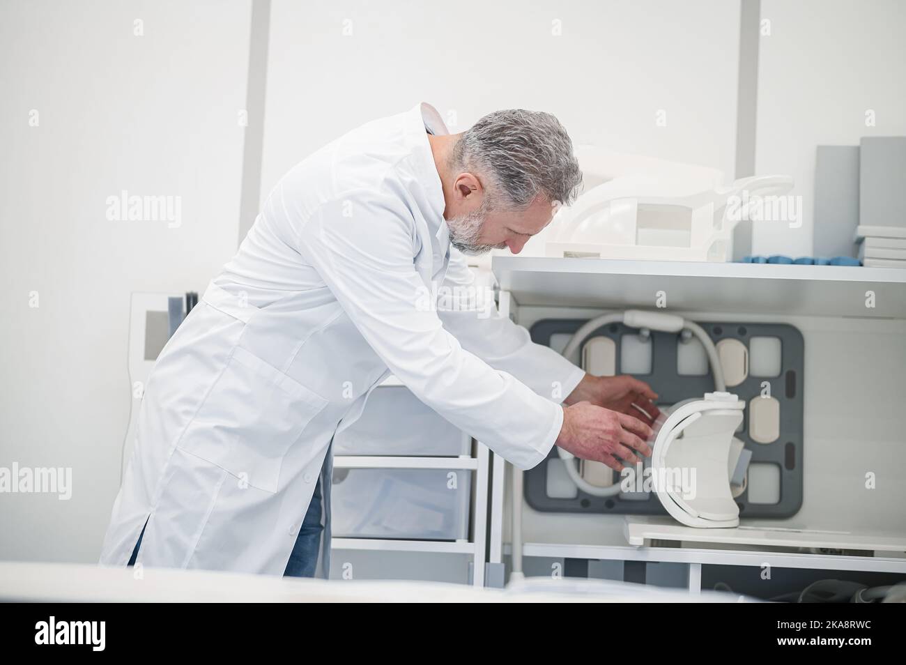 Male gray-haired doctor in a lab coat preparing MRI scanner Stock Photo