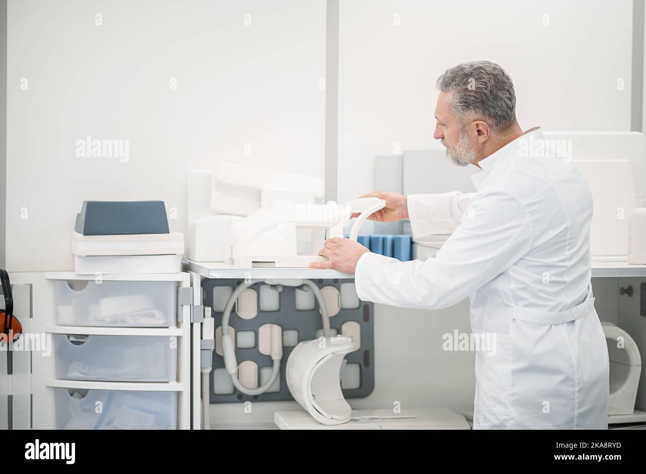 Male gray-haired doctor in a lab coat near MRI scanner Stock Photo